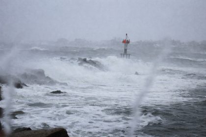 Rough waves crashing over rocks with a navigation marker visible in stormy conditions.